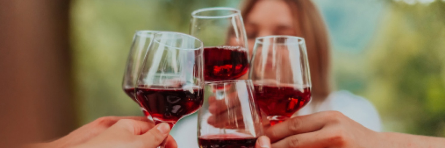 Drei Gläser Rotwein auf einem Holztisch, rote Weintrauben, Weingarten im Hintergrund