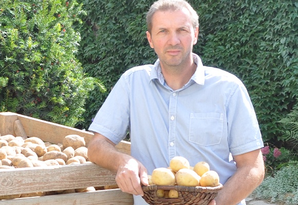 Mann in einem blauen Hemd mit kurzen Ärmeln steht neben einer Kiste Kartoffeln.
