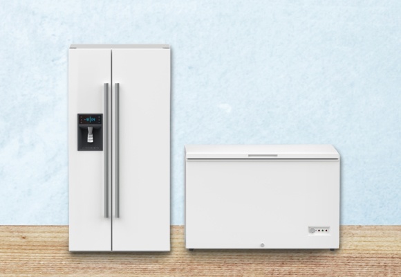 ein großer weißer Side by Side Gefrierschrank sowie eine weiße Gefriertruhe stehen auf einem Holzboden vor einer hellblauen Wand