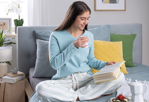 Ženska pižami sedi na postelji in bere knjigo