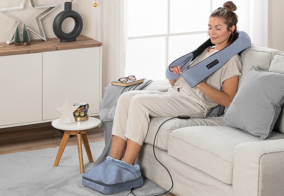 Ženska sedi na kavču uporablja napravo za masažo nog in vratu