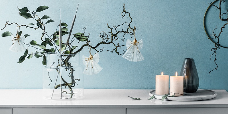 Blaue Wand, weiße Kommode mit Kerzen und eine Vase mit Ästen und Papierengeln als Deko