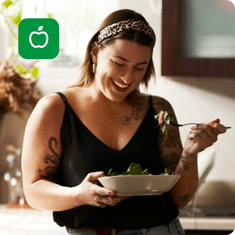 Eine junge Frau steht in der Küche. Sie isst mit einer Gabel Salat aus einer Schale.