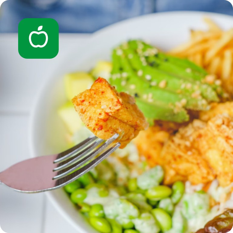 Gabel mit Tofu-Stück über einer farbenfrohen Salatschüssel mit Avocado, Edamame, Pommes und Blattsalat.