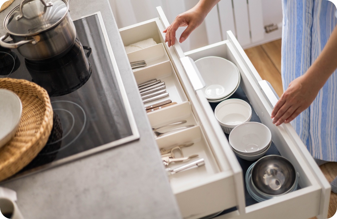 Person öffnet Küchenschubladen mit einsortiertem Besteck und Geschirr.