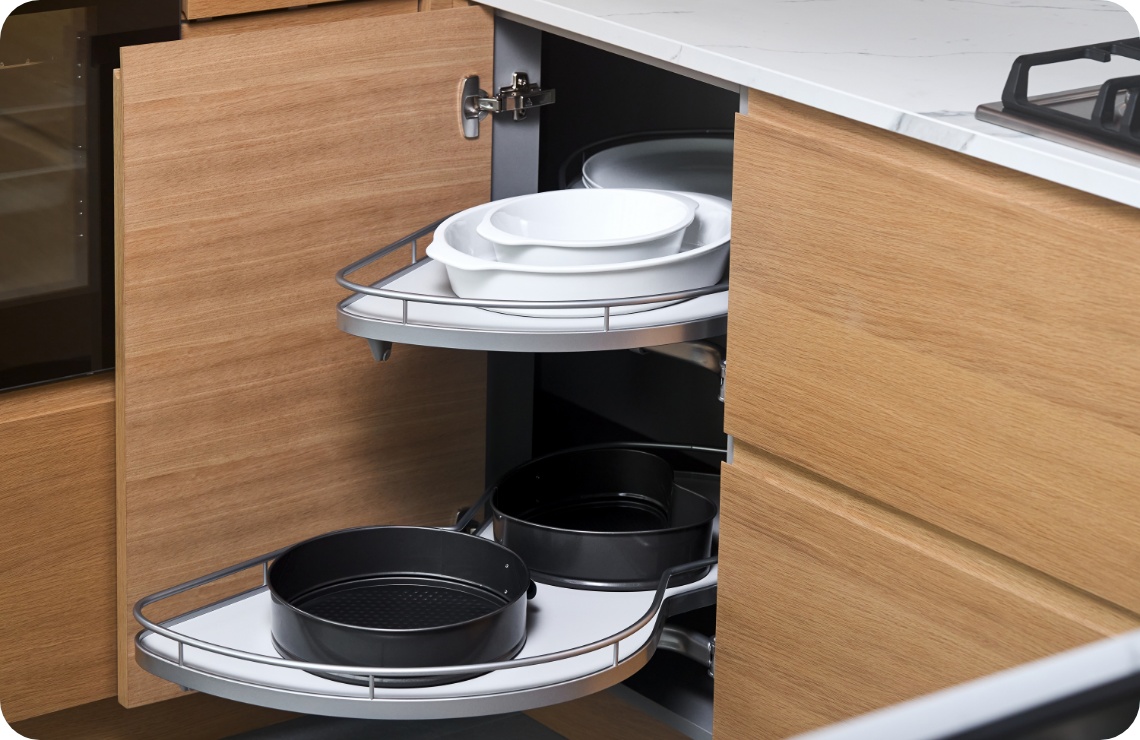 Geöffneter Eckschrank mit drehbarem Auszugssystem, gefüllt mit weißen Schüsseln und schwarzen Backformen.