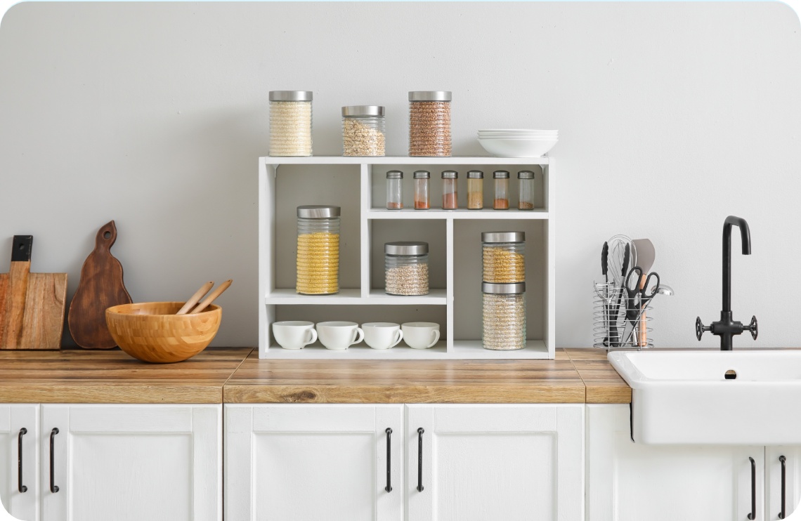 Minimalistische Küche mit weißem Regal, gefüllt mit Vorratsgläsern, Gewürzen, Tassen und Schüsseln auf Holzarbeitsplatte.