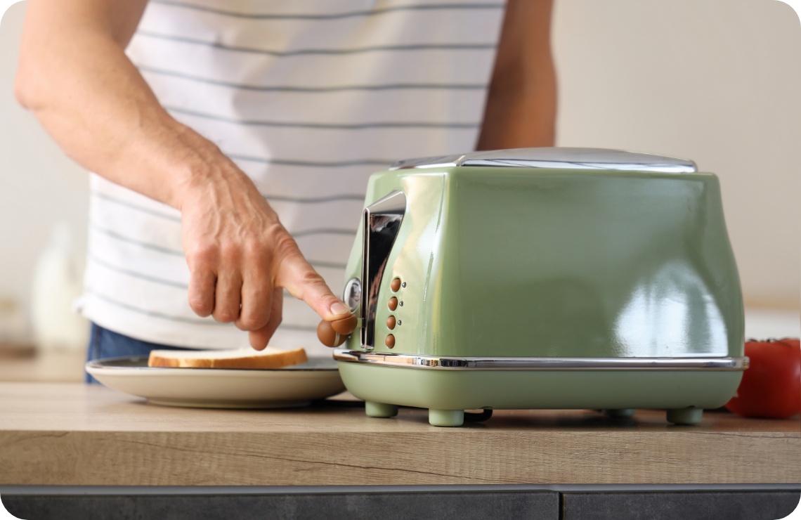 Person drückt den Hebel eines grünen Retro-Toasters, der auf einer Holzarbeitsplatte steht.