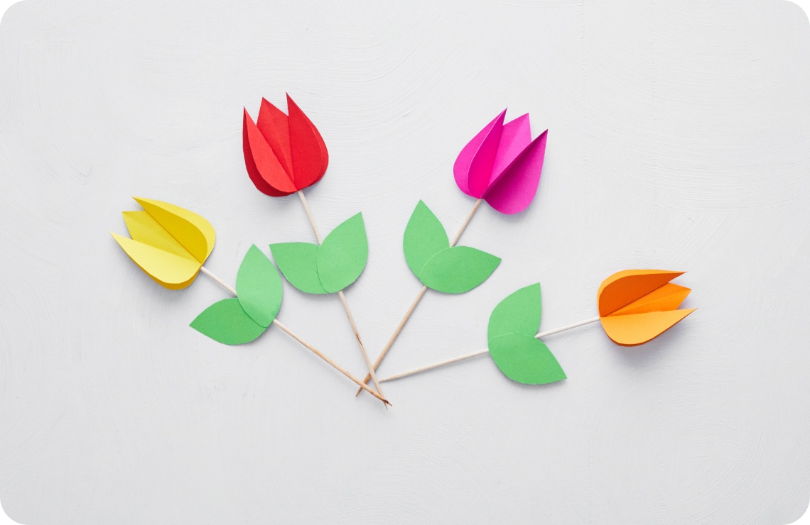 Bunte Tulpen aus Papier mit grünen Blättern auf Holzstäbchen, kunstvoll arrangiert auf weißem Hintergrund.