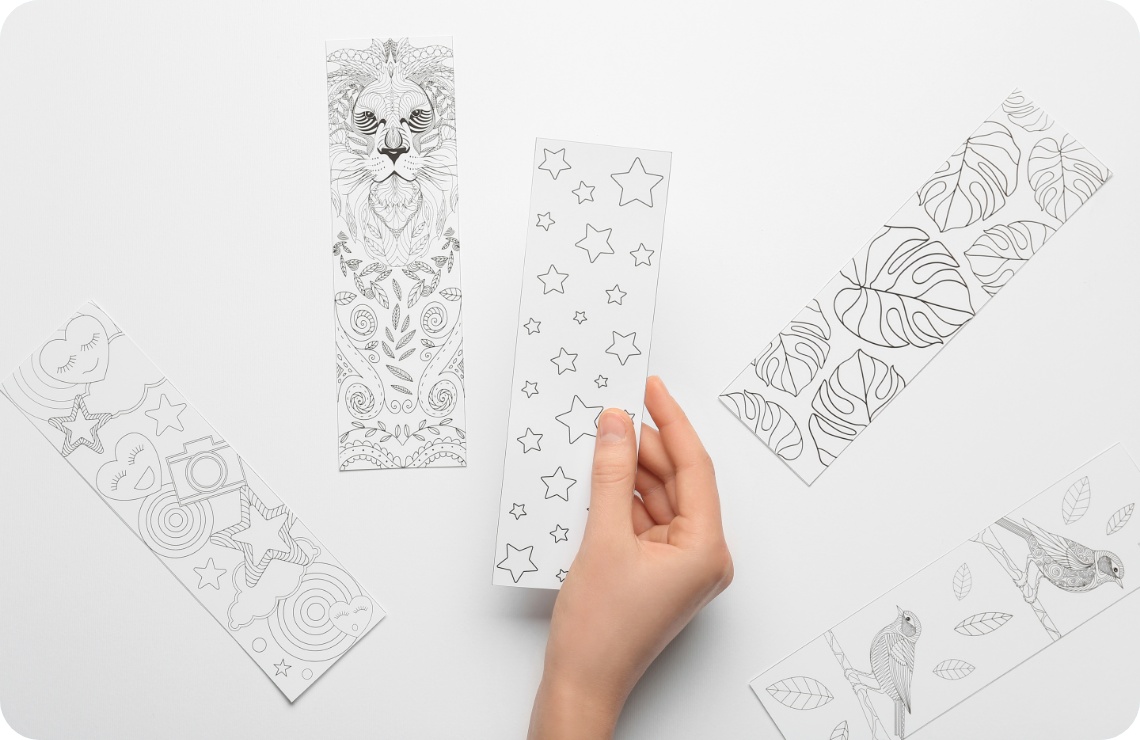 Hand hält ein Lesezeichen mit Sternenmuster. Umgeben von weiteren schwarz-weißen Lesezeichen mit Tier- und Pflanzenmotiven.