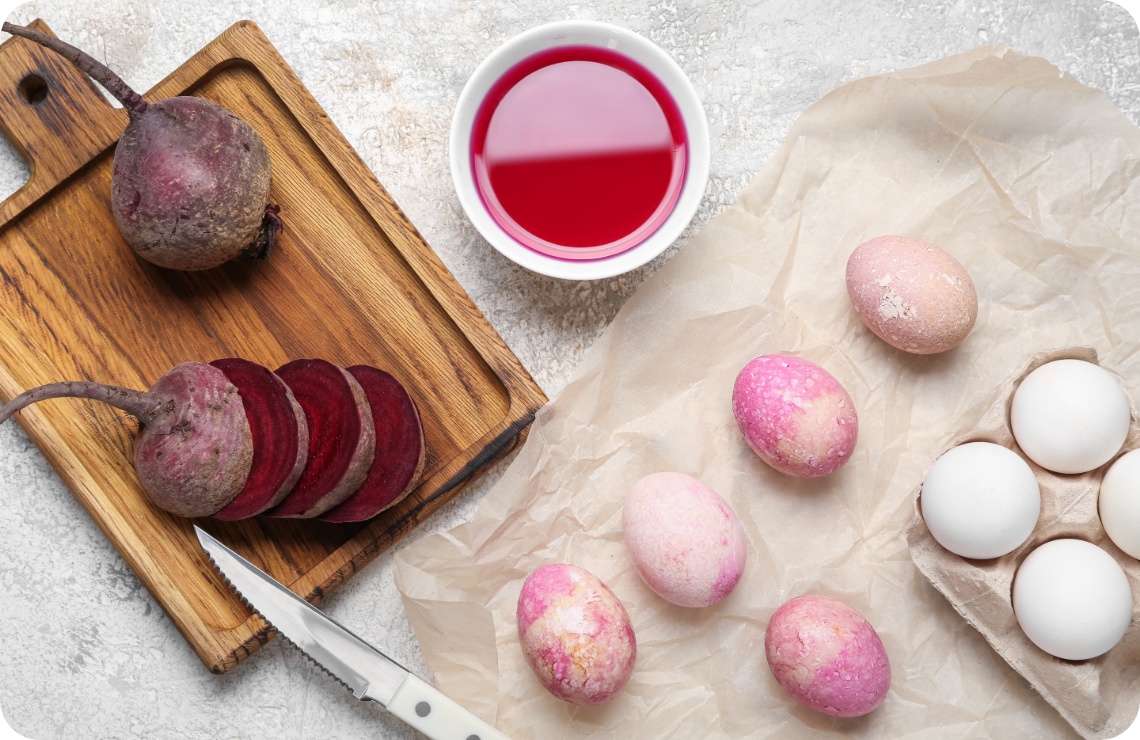 Natürlich gefärbte Ostereier mit Roter Bete auf Pergamentpapier. Daneben geschnittene Rote Bete, Messer und Rote-Bete-Saft.