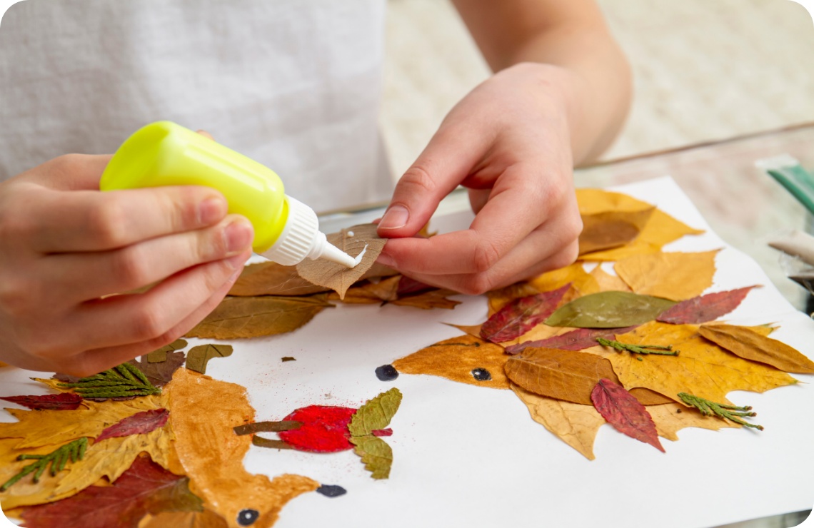 Kind bastelt ein herbstliches Bild mit getrockneten Blättern und Kleber. Kreatives DIY-Projekt mit Blätterkunst auf weißem Papier.