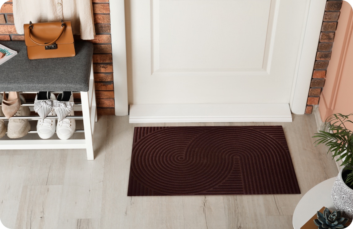 Eingangsbereich mit Welcome-Fußmatte, Schuhregal, grauer Bank und Tasche an der Wand.