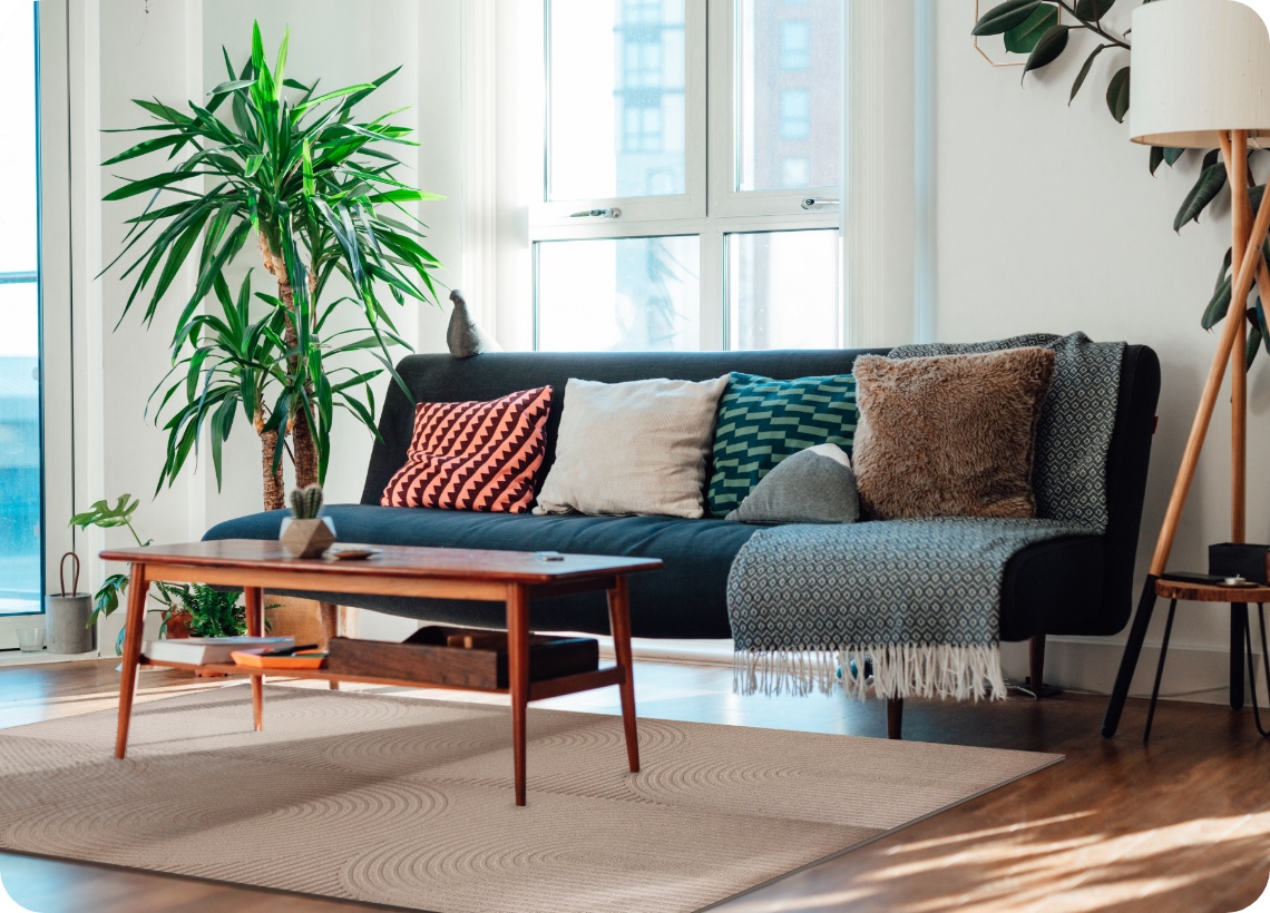 Modernes Wohnzimmer im Danish Design mit Pflanzen, Sofa mit Kissen, Holztisch, Stehlampe und mehreren ALDI Fußmatten als Teppich zusammengesetzt.