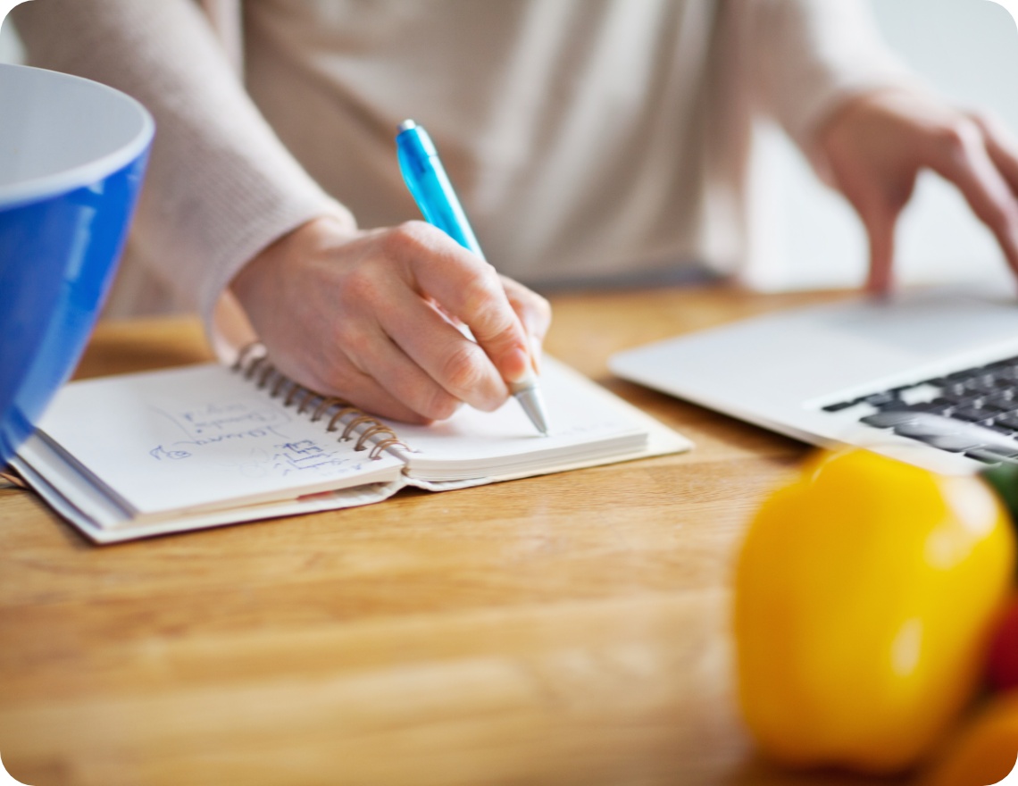 Person schreibt eine Einkaufsliste in ein Notizbuch.