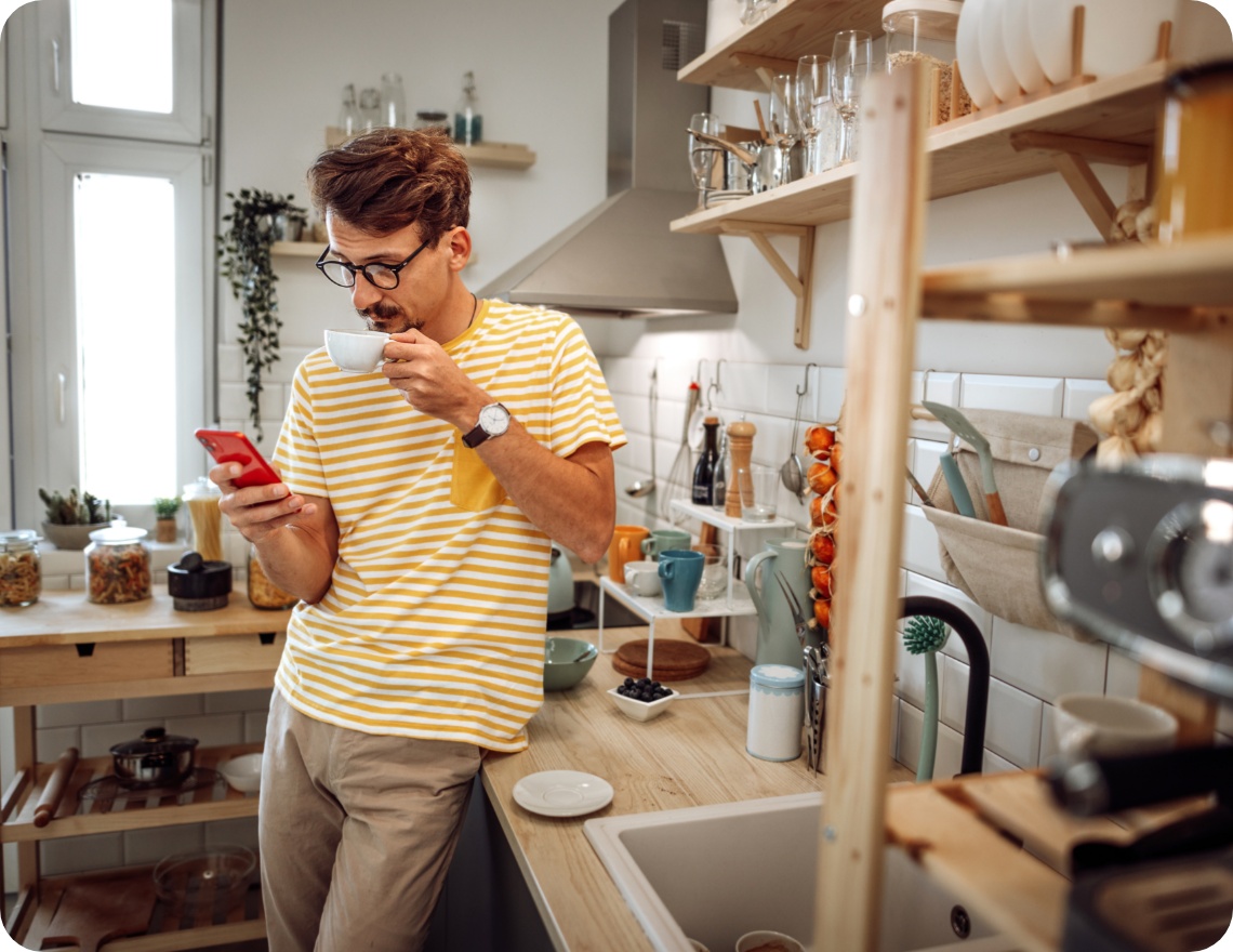 Mann in gestreiftem Shirt trinkt eine Tasse Kaffee und schaut in seinem Smartphone nach Sonderangeboten.