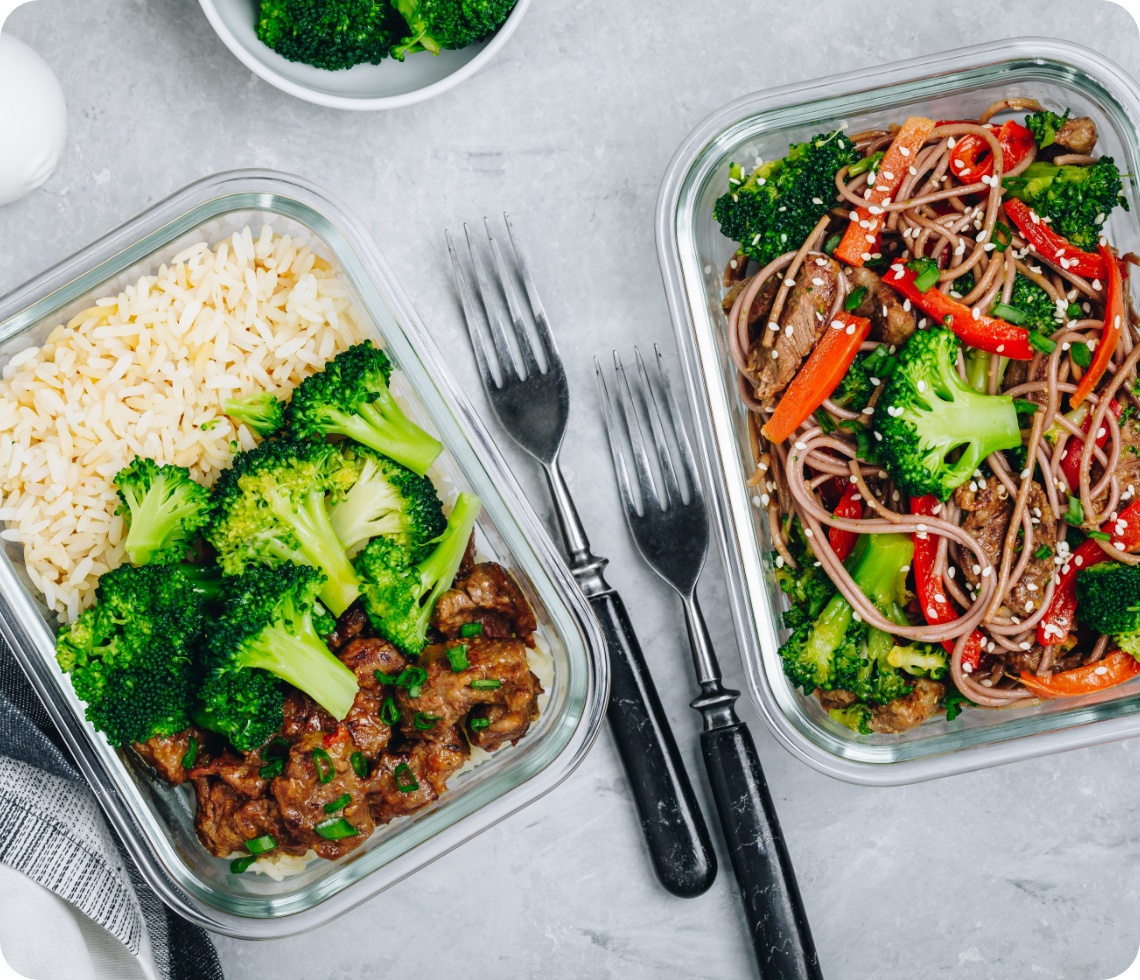 Zubereitetes Essen mit Reis, Gemüse und Vollkornudeln in zwei Glasschalen.