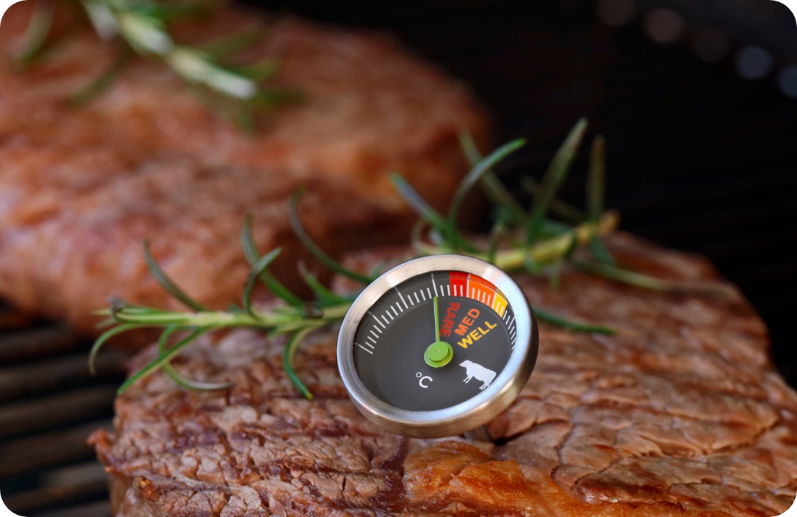 Medium gegrilltes Steak mit Fleischthermometer und Rosmarinzweig auf Grillrost, Temperaturanzeige gut sichtbar.