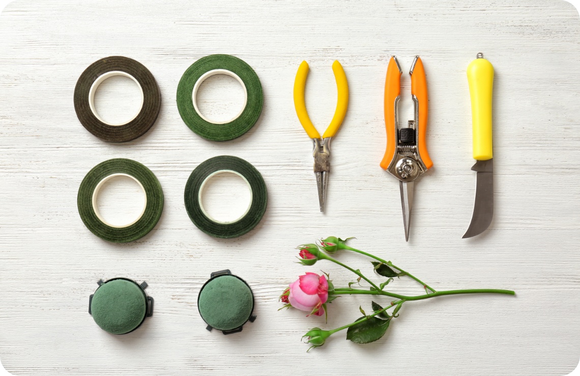 Klebeband, Schere, Messer und Steckschaum liegen bereit auf einer Tischplatte.