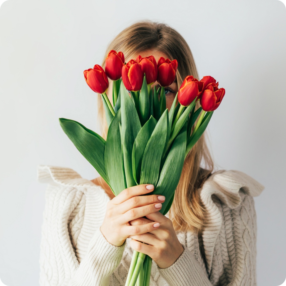 Eine Frau hält sich einen Strauß mit roten Tulpen vor ihr Gesicht.