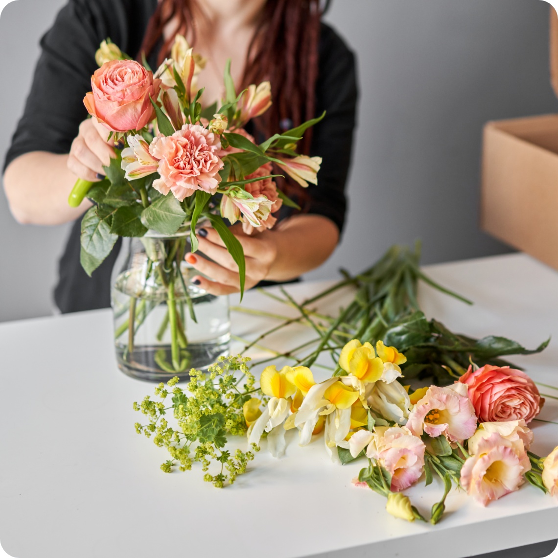 Frau steckt Frühlingsblumen in dern Farben gelb, oragen und rosa in eine durchsichtige Vase.