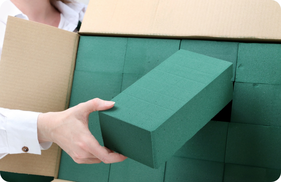 Person holt einen grünen Steckschaumblock aus einer Pappkiste.
