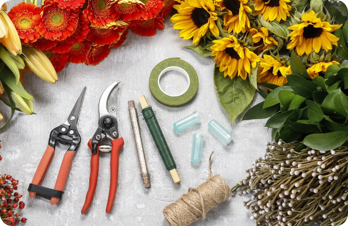 Gartenschere, Draht, Jurteband, Klebeband liegen it frischen Blumen auf einem Tisch.