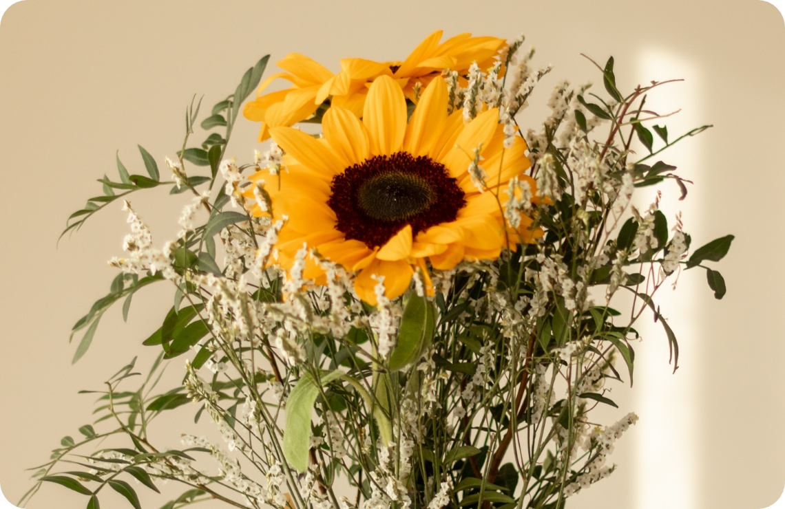 Person hält frischen Strauß mit Sonnenblumen und Grünzeug in der Hand.