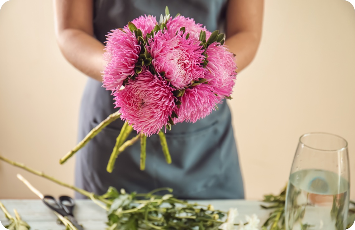Floristin bindet Strauß aus leuchtend pinken Chrysanthemen auf rustikalem Holztisch..