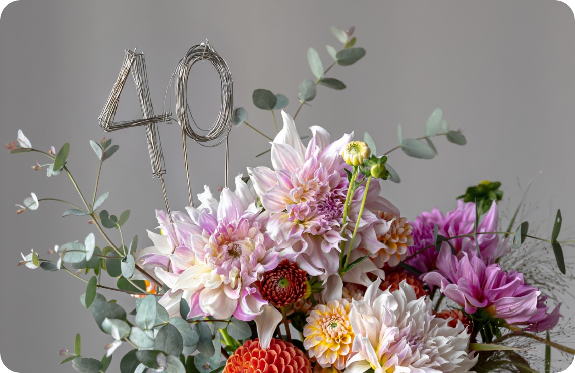 Festlicher Blumenstrauß aus bunten Dahlien, Eukalyptus und Draht-Dekoration mit der Zahl 40 vor grauem Hintergrund..