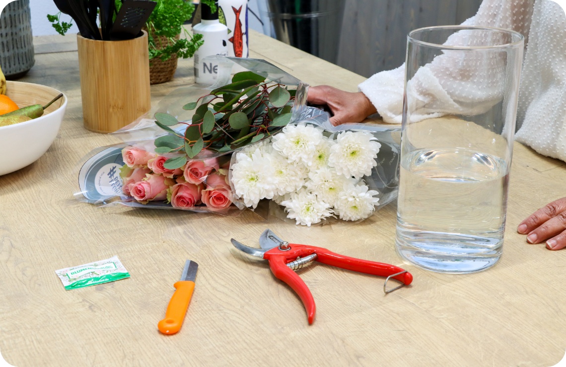 Frische Blumen, Vase mit Wasser und Materialien auf einem Tisch.