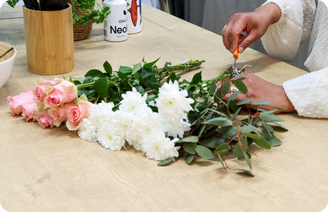 Person entfernt die Blätter von rosa Rosen und weißen Chryanthemen, die auf einer Tischplatte liegen.