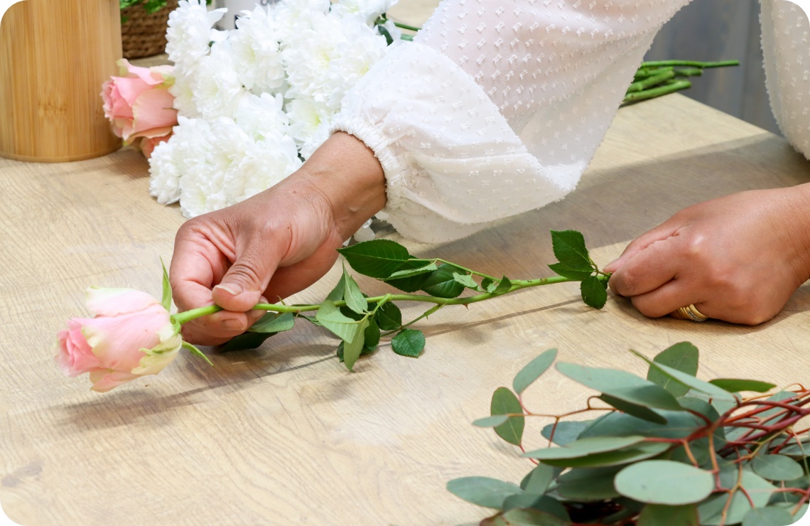 Person legt einen Rosenstiel vor sich auf die Tischplatte.