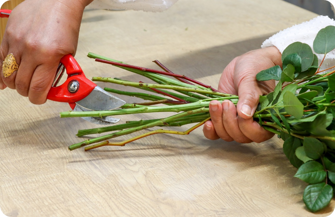 Person kürzt Blumenstiele mit einem Messer.