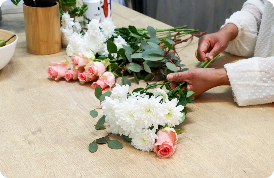 Person sortiert rosa Rosen und weiße Chrysanthemen auf einer Tischplatte.
