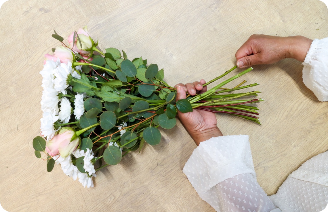 Person bindet Blumenstrauß an den Stielen zusammen.