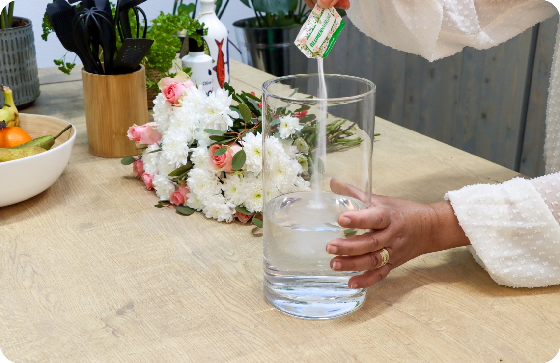 Person gibt Blumenfrisch in eine mit Wasser gefüllte Vase.