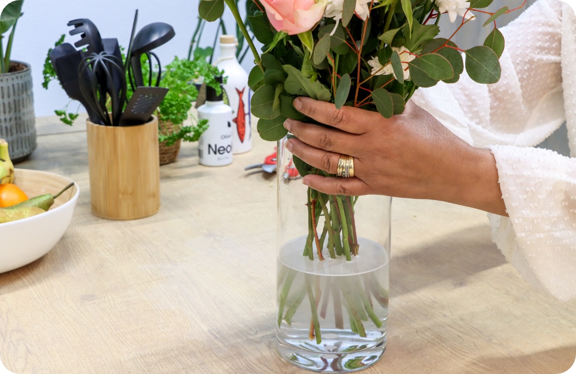 Person stellt gebundenen Blumenstrauß in eine mit Wasser gefüllte Vase.