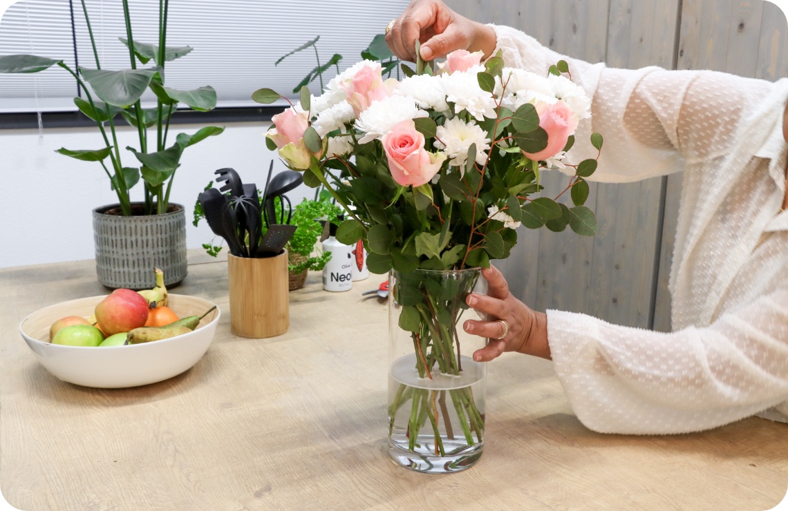 Person rückt Blumenstrauß der in einer Vase steht zurecht.
