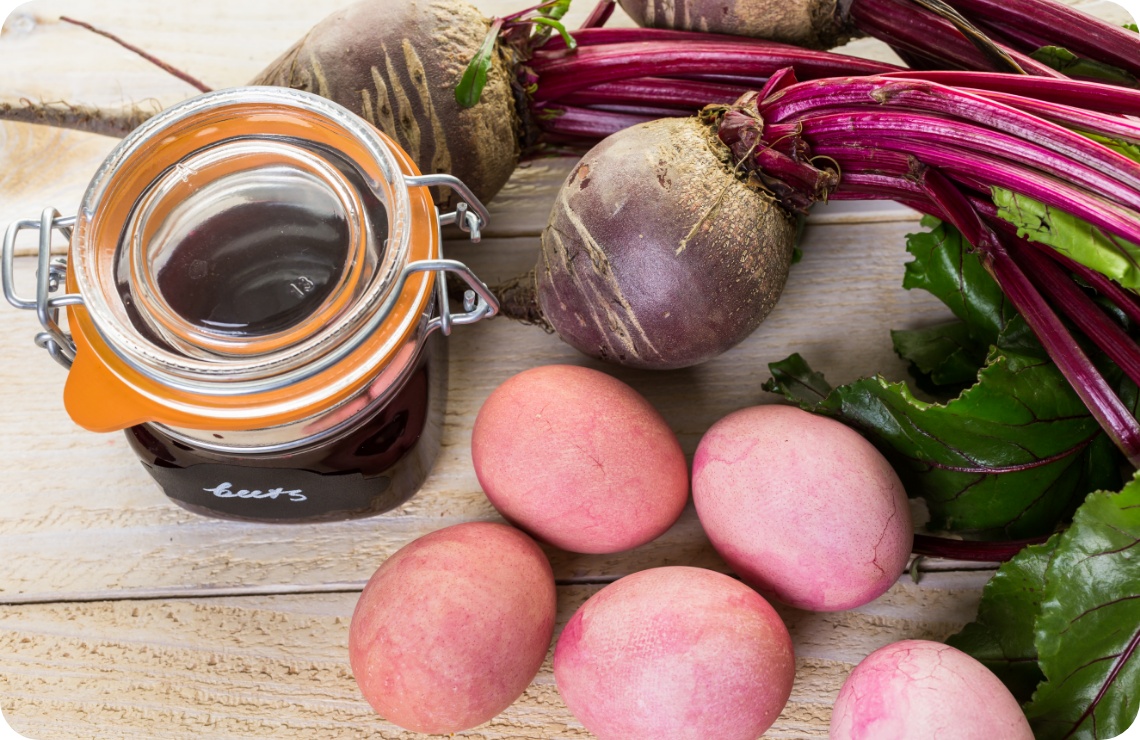 Natürlich gefärbte rosa Ostereier, Rote Bete und ein Glas Rote-Bete-Farbsud auf rustikalem Holztisch.