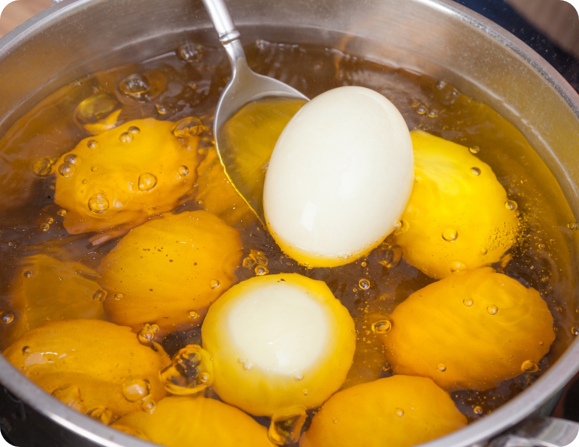 Kochtopf mit sprudelndem Wasser, in dem ungeschälte Eier gelb gefärt werden.