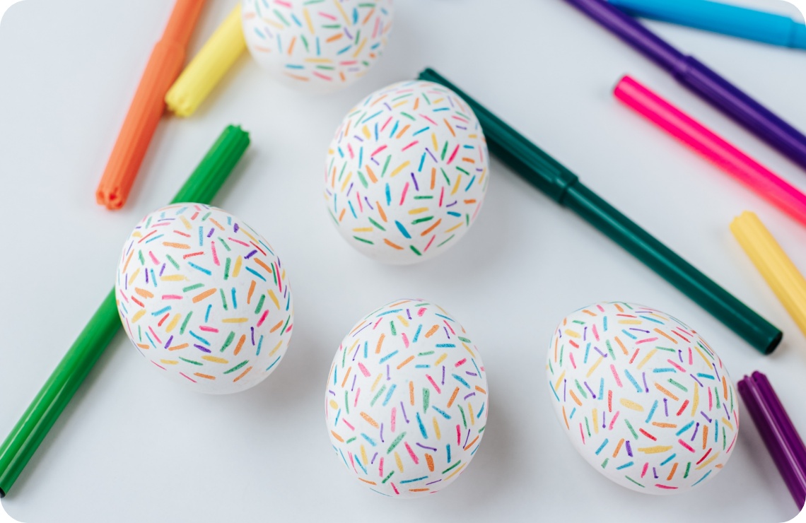 Weiße mit Filzstiften bemalte Ostereier mit bunten Strichmustern.