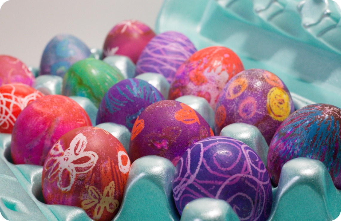 Farbenfroh verzierte Ostereier mit Mustern in einer türkisfarbenen Eierverpackung, kreativ gestaltet in Rot, Lila und Blau.