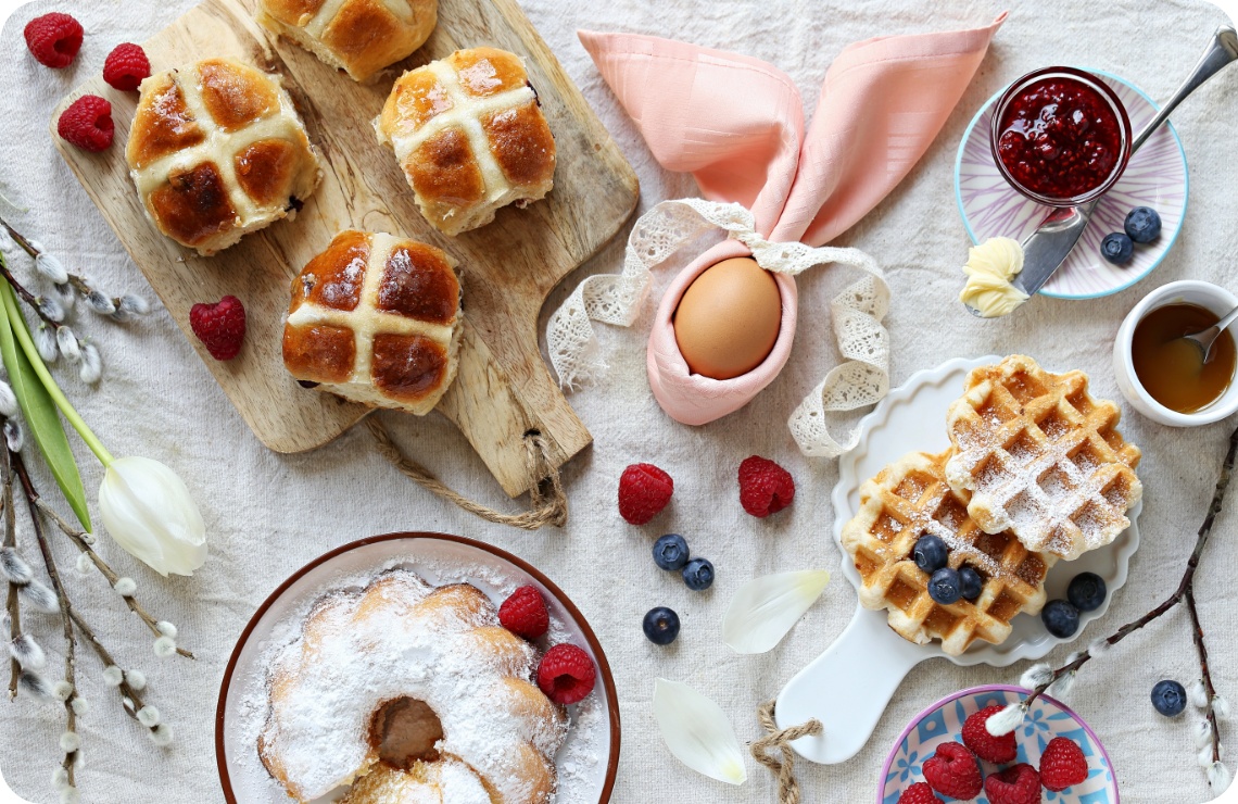 Kuchen, Waffeln, Eier und süßes Ostergebäck stehen auf einem Tisch für den Osterbrunch bereit.