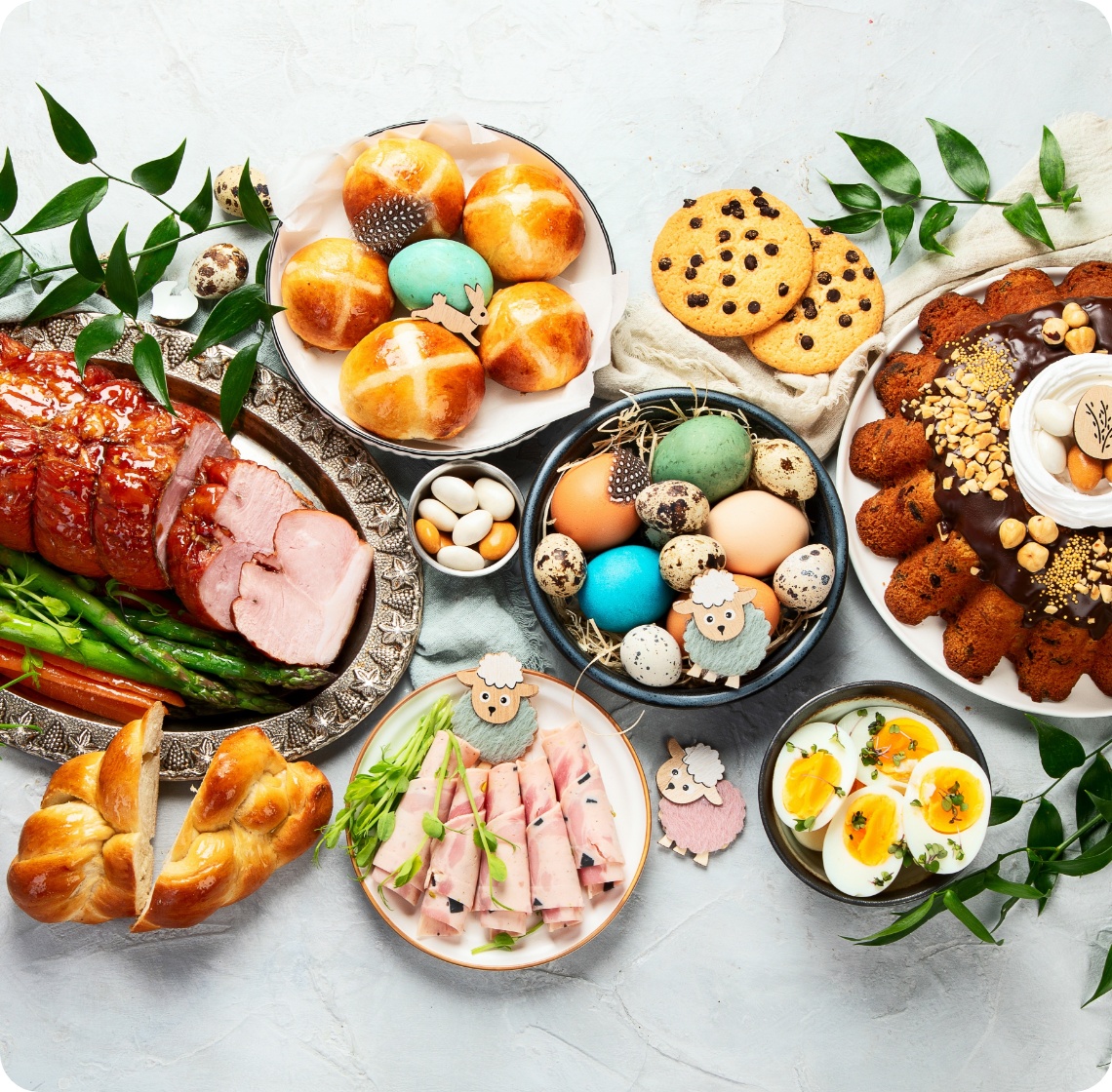 Osterbrunch mit glasiertem Schinken, bunt gefärbten Eiern, Hefezopf, Kuchen, Brötchen, Schinkenröllchen und Keksen.