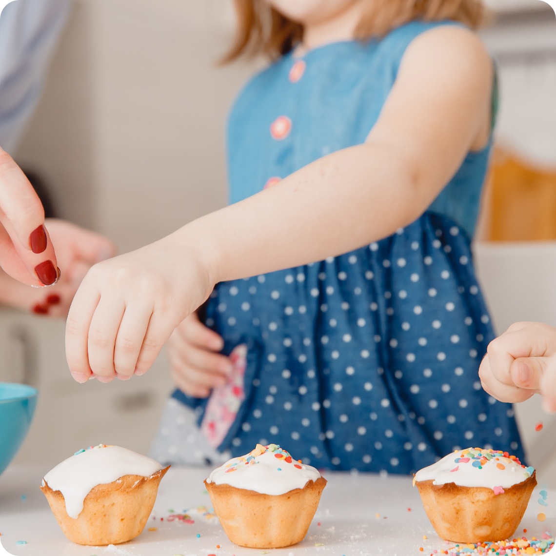 Kinder dekorieren Muffins mit Zuckerguss und bunten Streuseln beim gemeinsamen Osterbacken in der Küche.