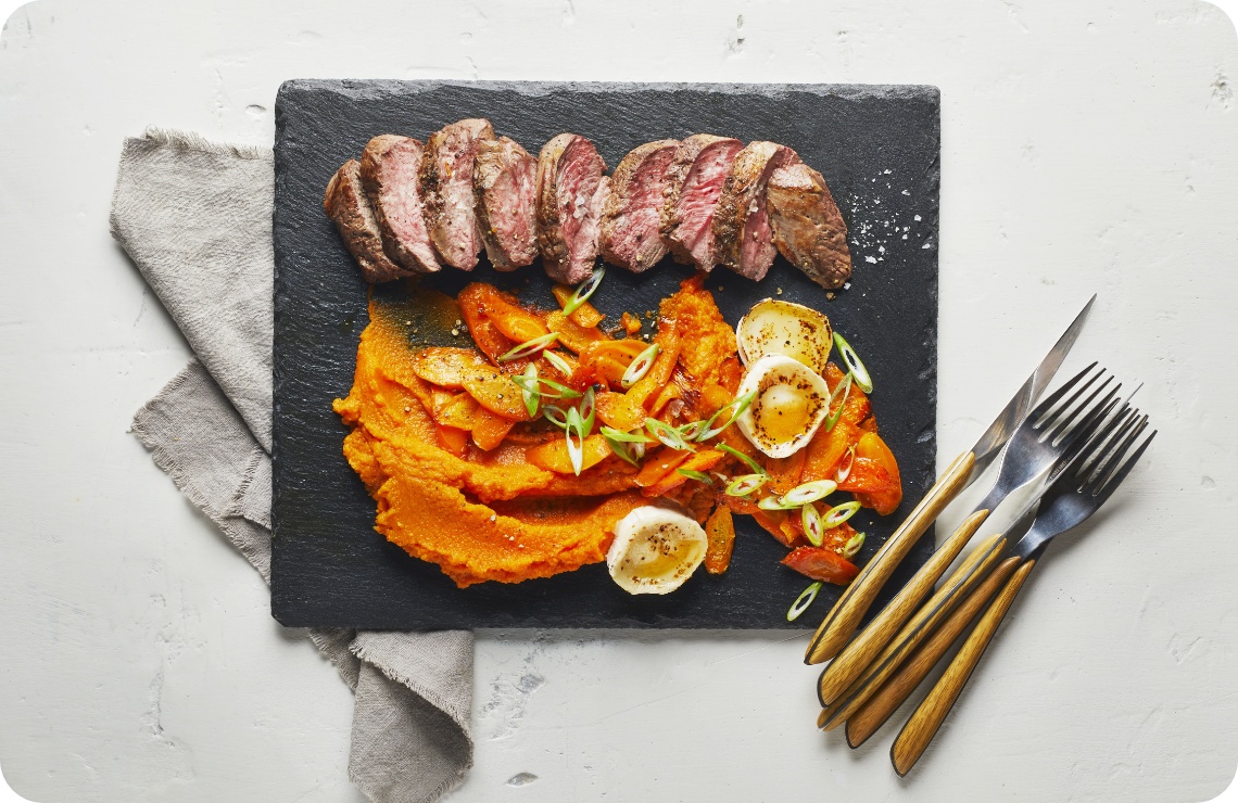 Als Hauptgericht zu Ostern liegt ein gebratenes Lammsteak aufgeschnitten und mit etwas Möhrenpüree als Beilage auf einer Schieferplatte