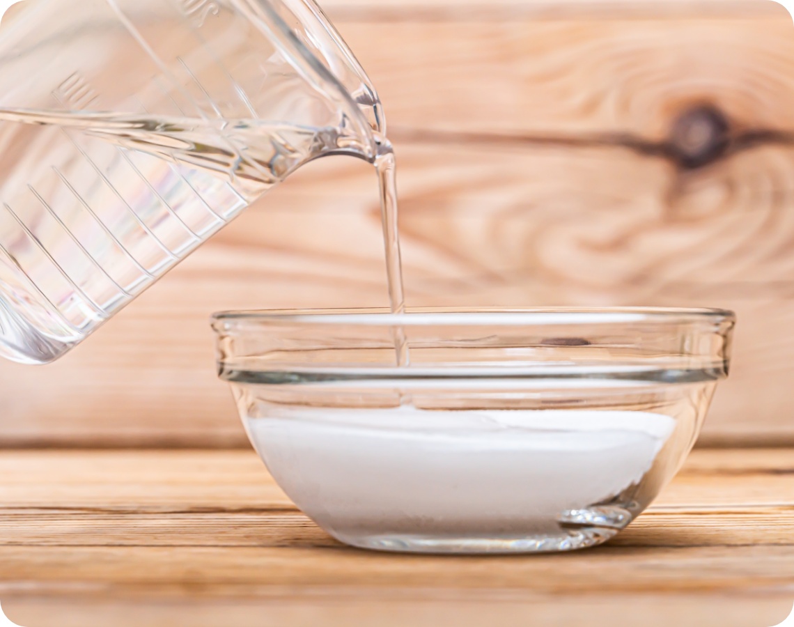 Nahaufnahme wie Essig aus einem Messbecher in eine Glasschale mit Natron gegossen wird.