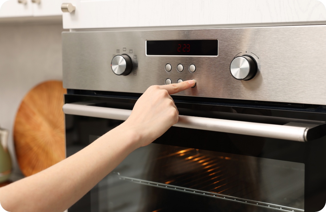 Person drückt die Taste eines modernen Edelstahl-Backofens mit digitaler Anzeige in einer Küche.