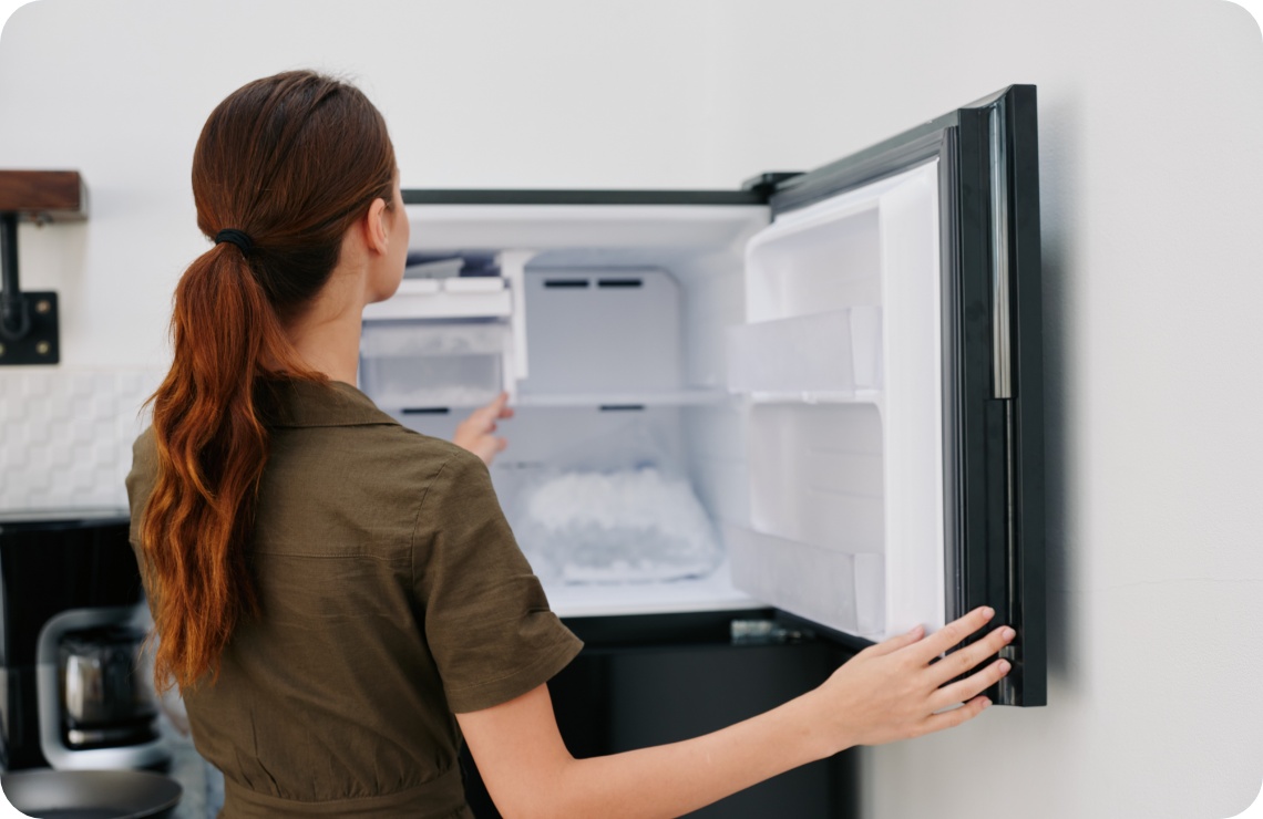 Frau öffnet einen mit Eiswürfeln gefüllten Gefrierschrank in einer modernen Küche.